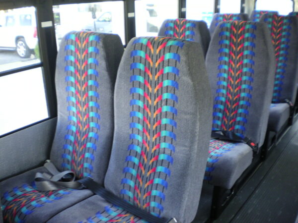Bus interior with gray seats featuring blue, red and teal woven patterns as part of the upholstery mixbed.
