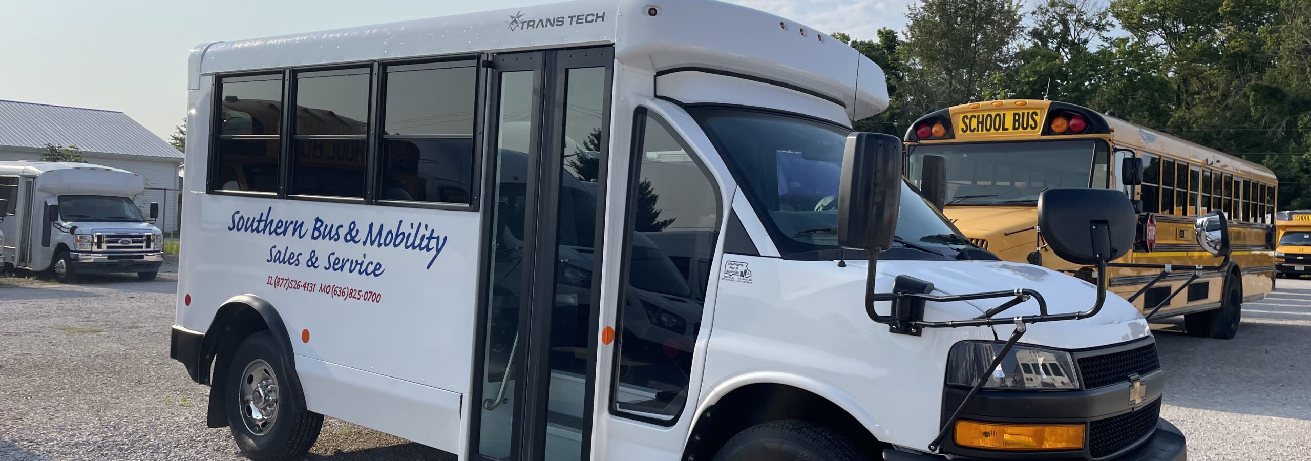 White passenger bus with an open side door in a parking lot, branding reads 'Southern Bus & Mobility Sales & Service'; yellow school bus visible in the background against a blue sky.