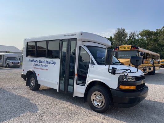 White passenger bus with an open side door in a parking lot, branding reads 'Southern Bus & Mobility Sales & Service'; yellow school bus visible in the background against a blue sky.