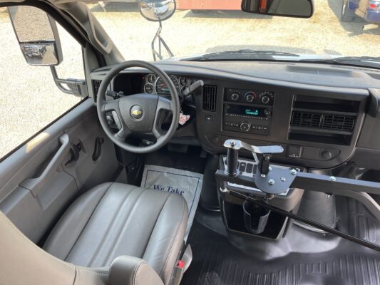 Interior view of a Chevrolet truck cab showing steering wheel, instrument cluster, center dash controls, and a metal mounting rig near the passenger area; side mirror visible through the window.