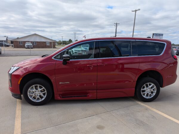 Red SUV parked in a lot with a chain-link fence and a brick building in the background under a cloudy sky, BraunAbility logo visible on the side.