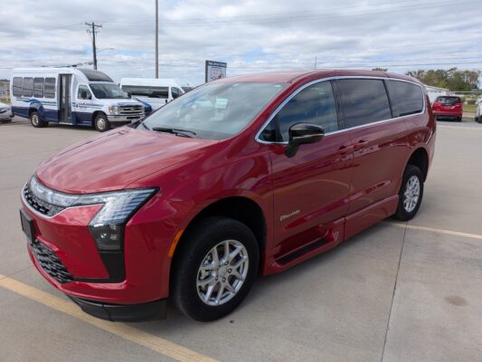 Red minivan in the foreground with white shuttle buses visible in a parking lot and cloudy sky behind.