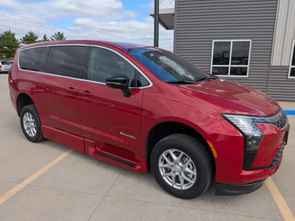Red BraunAbility minivan parked in a lot next to a gray metal building, showing side and front with tinted windows and chrome trim.