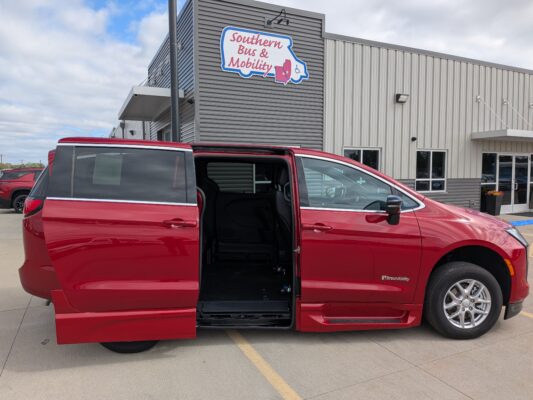 Red wheelchair-accessible van with its sliding door open in a parking lot, outside a building with 'Southern Bus & Mobility' sign in view.