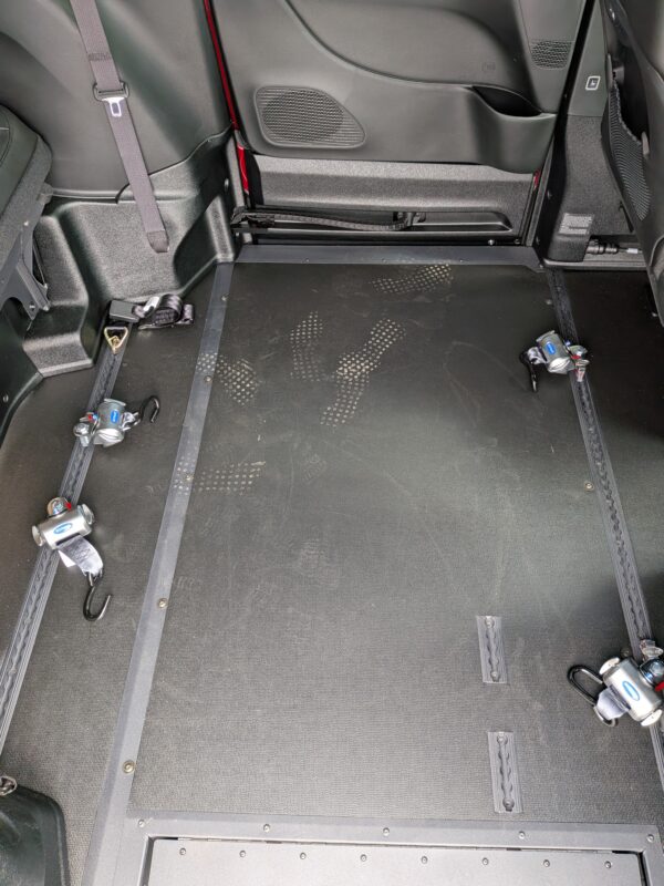 Wheelchair-accessible van interior showing a flat floor with strap-down anchors and side rails for securing a wheelchair.