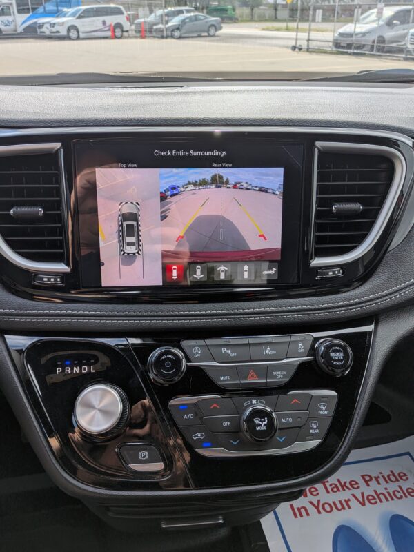 In-dash rearview camera display showing top-down and rear parking views with guiding lines as the car backs into a parking lot.
