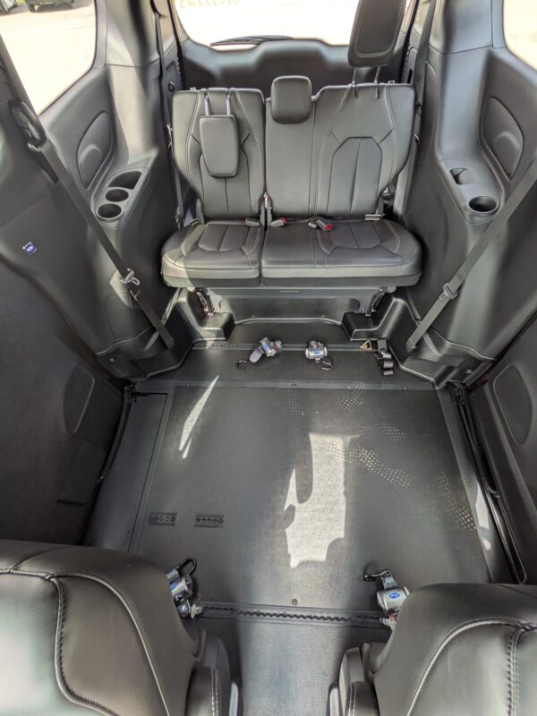 Two black leather rear captain seats with headrests and visible seat belts in a vehicle interior, cup holders on the side panels behind them