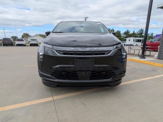 Front view of a dark SUV parked in a lot with other cars in the background on a cloudy day.