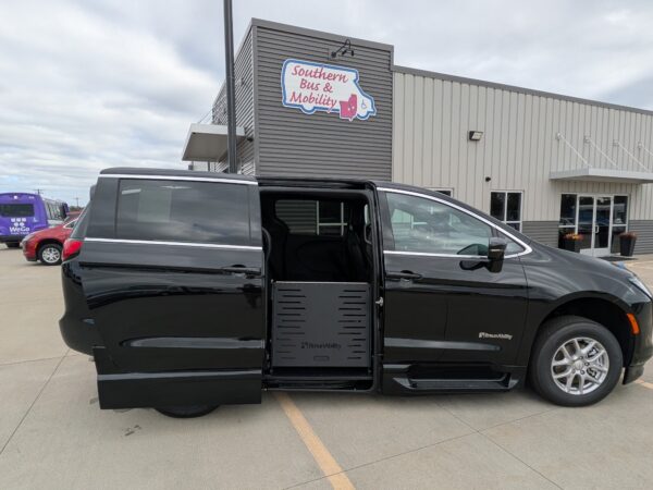 PXL_20260922_201301832 Black BraunAbility wheelchair van with its side-entry ramp deployed in a parking lot near a mobility store building.