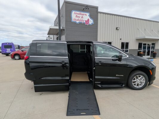 Black BraunAbility wheelchair-accessible van with its side ramp deployed in a parking lot in front of a Southern Bus & Mobility building.