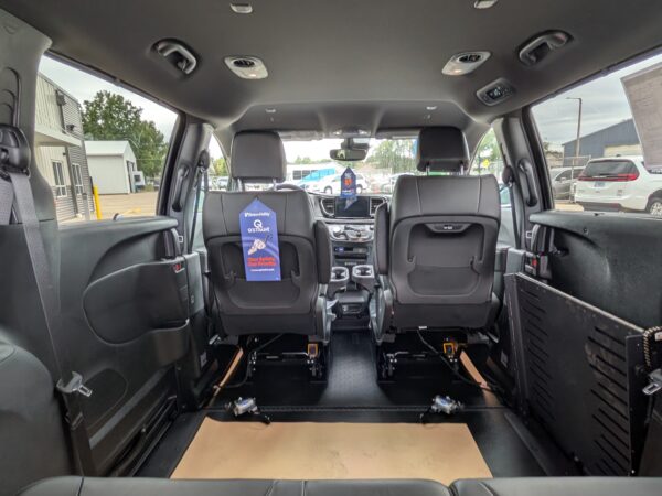 PXL_20260922_201330817 Interior of a wheelchair-accessible van with rear seats removed, exposing a wooden ramp floor and mounting rails toward the front dashboard.
