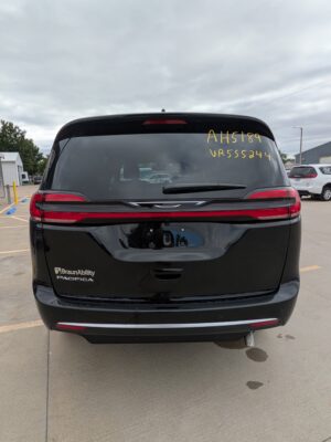 Rear view of a black BraunAbility Pacifica minivan in a parking lot, with yellow writing on the rear window (AH5189 VR55524). The vehicle has red tail lights and a rear wiper.