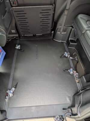 Interior of a vehicle’s rear area with a folded backrest/panel, exposed floor anchors, and visible seat belts on the sides