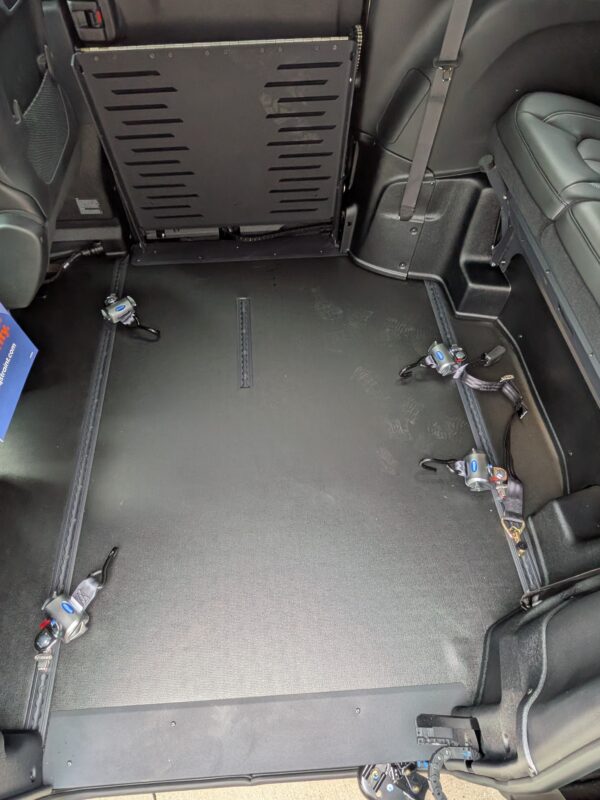 PXL_20260922_201403086 Interior of a vehicle’s rear area with a folded backrest/panel, exposed floor anchors, and visible seat belts on the sides