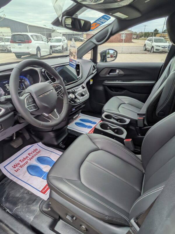 PXL_20260922_201428654 Interior of a car showroom vehicle: black leather driver and front passenger seats, steering wheel, and center console with a floor mat reading 'We Take Pride In Your Vehicle.'