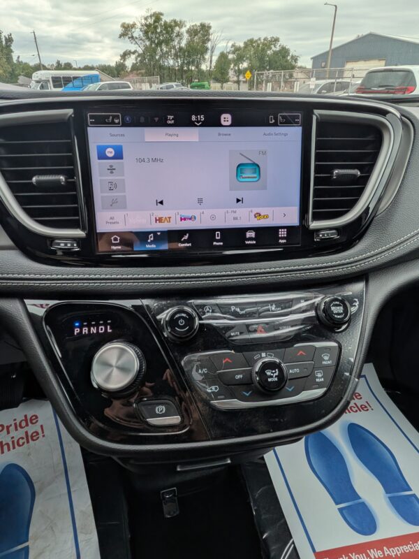 PXL_20260922_201514038 Car dashboard with a large touchscreen displaying FM radio and 104.3 MHz, surrounded by climate controls and glossy black trim.