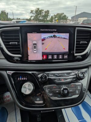 Car dashboard with a touchscreen showing rear and top-down parking camera views and guide lines in a parking lot.