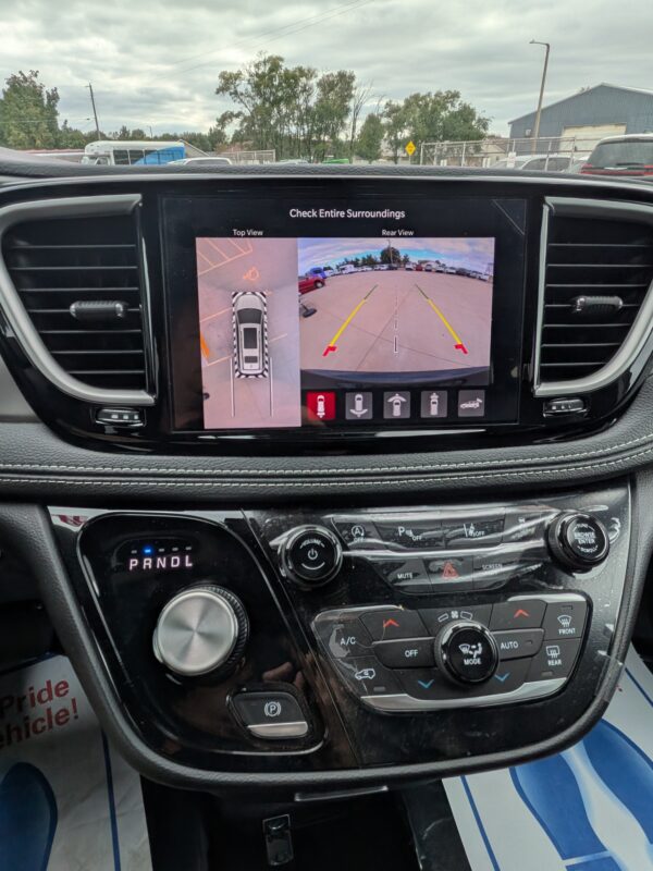 PXL_20260922_201521758 Car dashboard with a touchscreen showing rear and top-down parking camera views and guide lines in a parking lot.