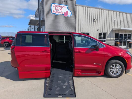 Red wheelchair-accessible van with its deployed side ramp in a parking lot outside a mobility store.