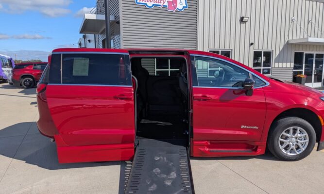 Red wheelchair-accessible minivan with a lowered ramp extended for boarding at a dealership