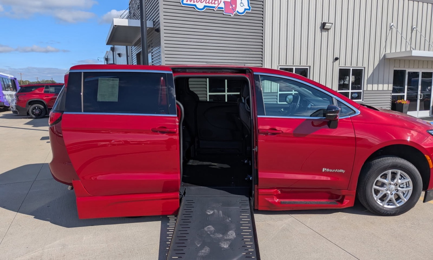 Red wheelchair-accessible minivan with a lowered ramp extended for boarding at a dealership