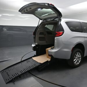 Silver minivan with rear hatch open, ramp extended to the floor, and a box inside the cargo area on a service lift.