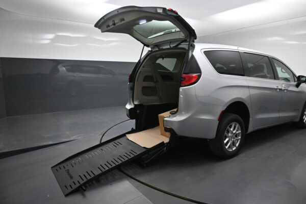Silver minivan with rear hatch open, ramp extended to the floor, and a box inside the cargo area on a service lift.