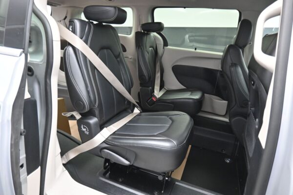 Two black leather captain's chairs with beige seat belts inside a minivan, showing middle-row seating and interior panels.