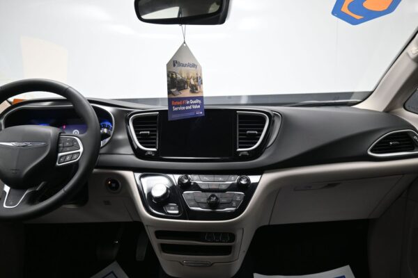 Front interior of a car showing the steering wheel, central touchscreen, climate controls, and a BraunAbility tag hanging from the rearview mirror.