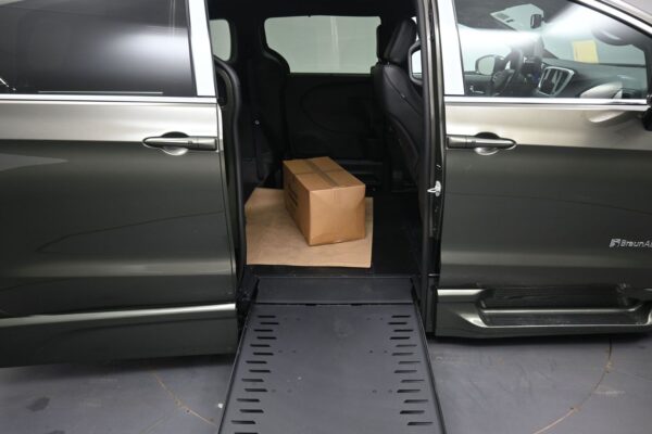 Wheelchair-accessible van with the side doorway open and a loading ramp extended, a cardboard box placed inside on the floor.