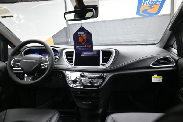 Front interior of a car showing the steering wheel, central infotainment display, and hanging 'Built to Trust' tag from the rearview mirror