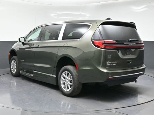 Rear three-quarter view of a green-gray Chrysler Pacifica minivan parked indoors, showing tail lights and bumper detail.