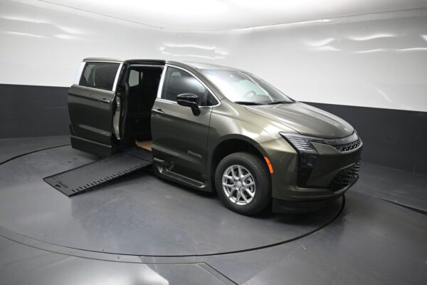 Olive-green minivan with a side-entry ramp extended, door open, displayed on a turntable in a showroom, highlighting accessibility features.