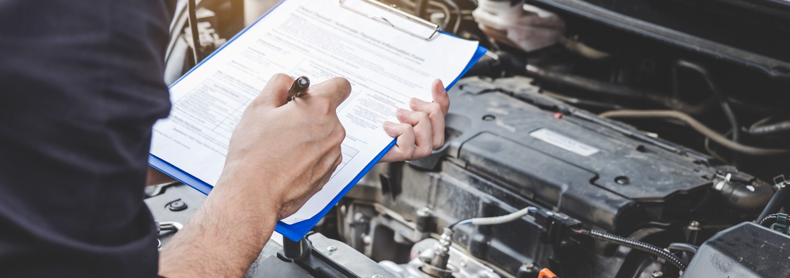 Automobile mechanic repairman checking a car engine with inspecting writing on the clipboard checklist for car service and maintenance.