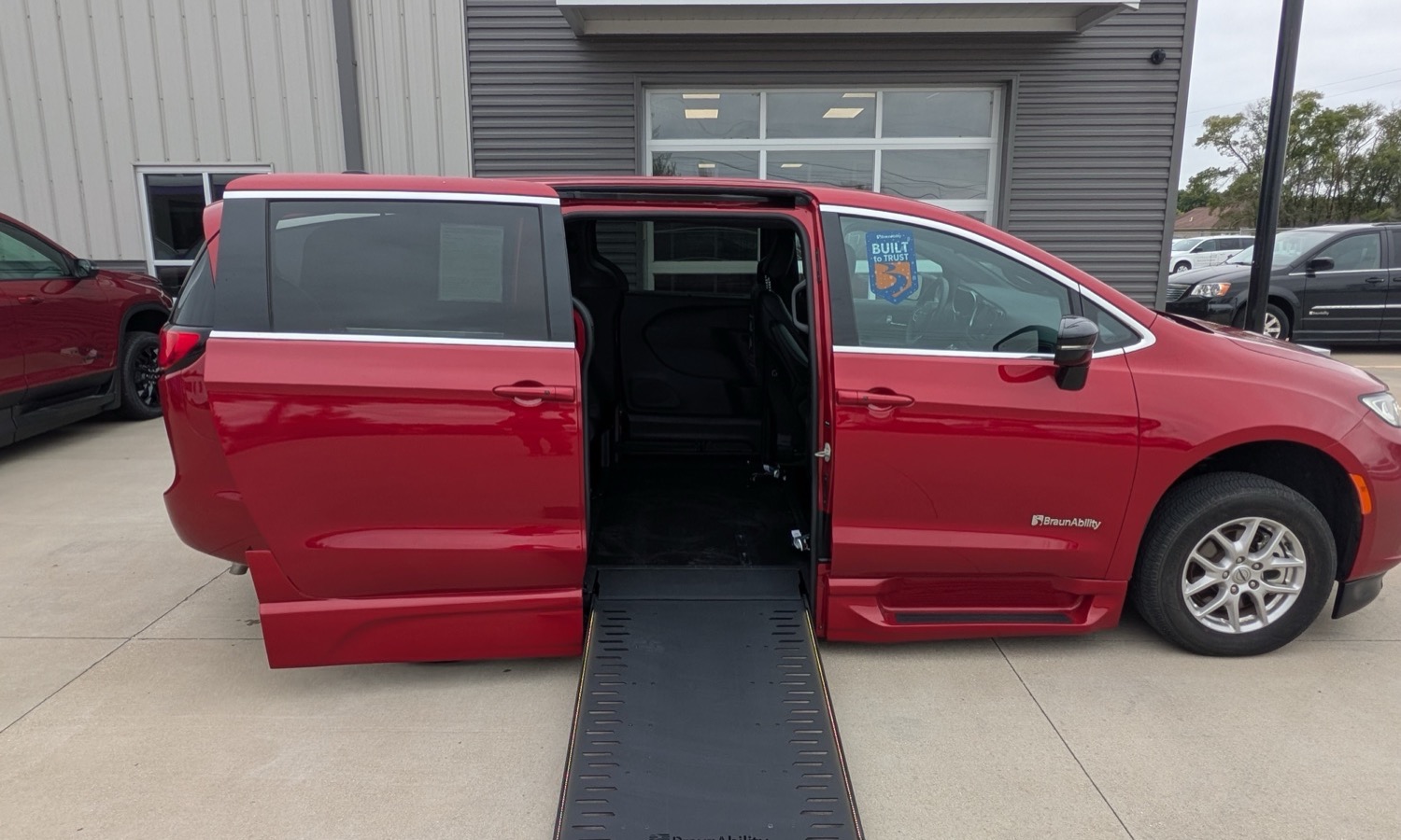 Red BraunAbility wheelchair-accessible van with ramp deployed and side door open, interior visible.