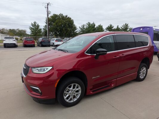 Red SUV/minivan in the foreground with BraunAbility logo, parked in a lot; other cars and a purple bus are in the background under an overcast sky