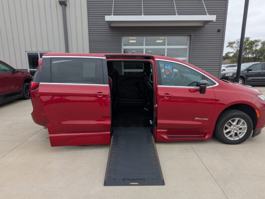 Red BraunAbility minivan with a lowered ramp extended to the ground in a dealership parking lot.
