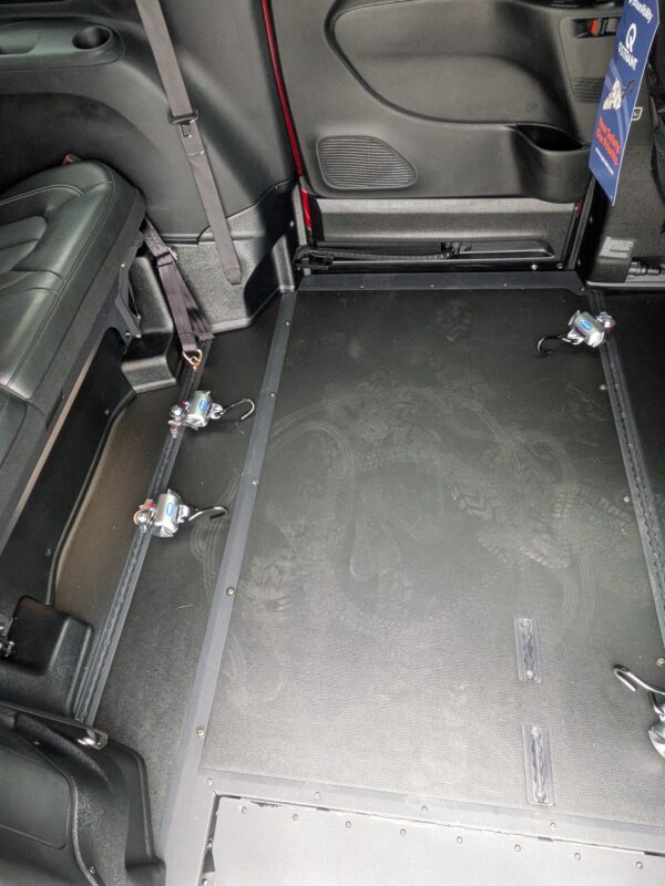 PXL_20260922_161150625 Interior of a vehicle showing a black floor with metal track rails, seat bases, and visible seat belts near the seat backs.